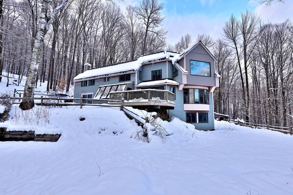 Une maison à deux étages avec un balcon, entourée d’arbres couverts de neige.