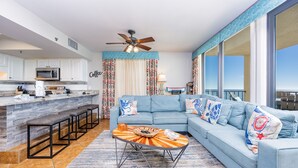 A modern living room with a light blue sofa, a coffee table, and a kitchen area with white cabinets and a microwave.