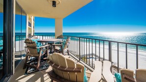 A balcony with a table and chairs, overlooking a beach with a clear view of the ocean.