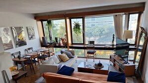 A modern living room with a sofa, dining table, and a large window with a city view.