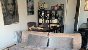 A living room with a grey sofa, a coffee table with a magazine, a bookshelf, and a radiator.