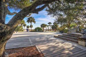 A wooden boardwalk leading to a beach area with palm trees and a staircase.