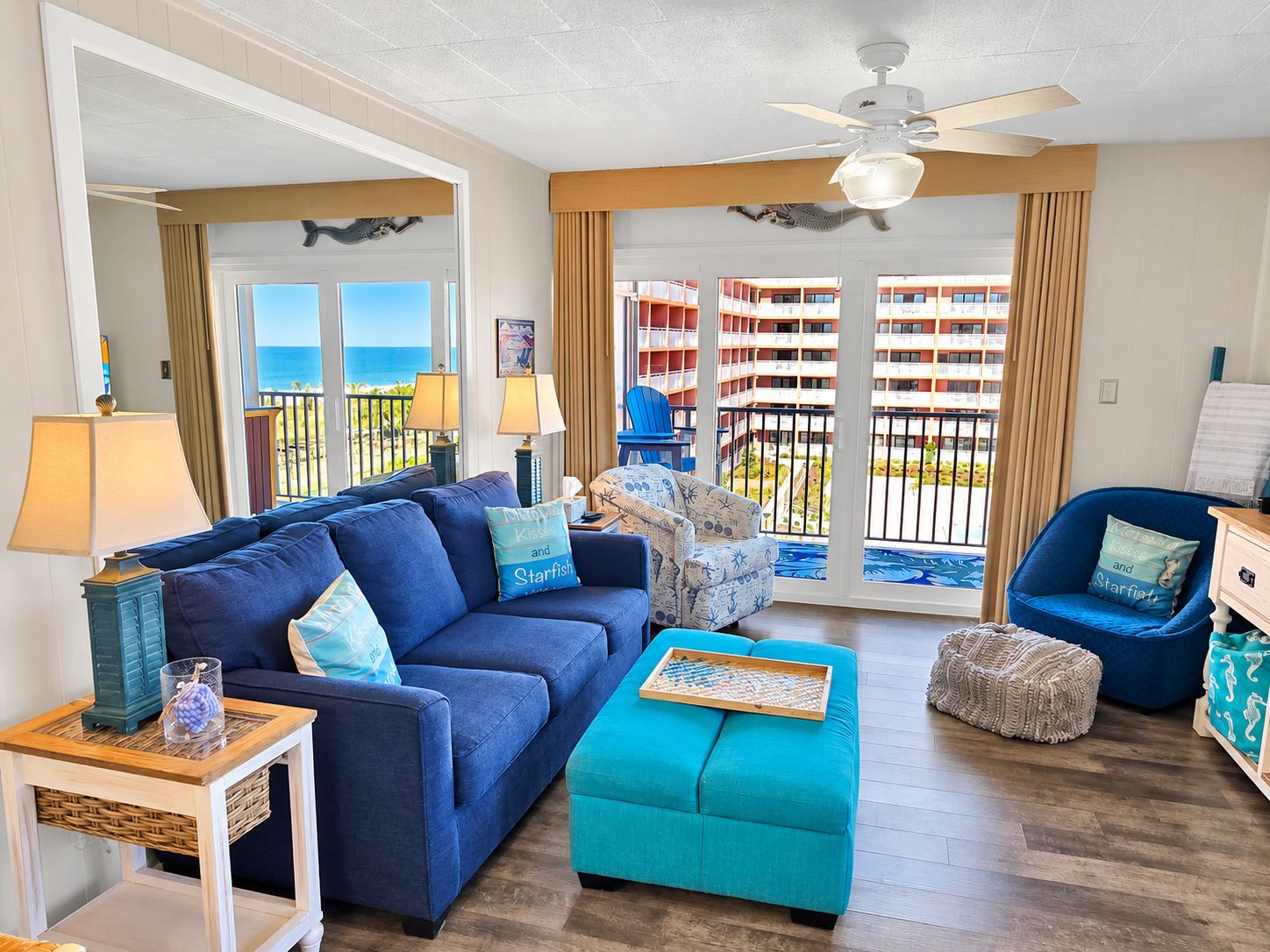 A living room with a blue sofa, a teal ottoman, and a ceiling fan.