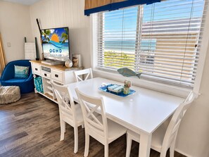 A room with a white table, white chairs, a television, and a window with blinds.