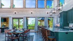 A spacious dining area with a high ceiling and large windows, wooden flooring, and a view of the outdoors.