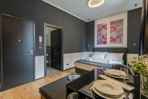 A modern hotel room with a bed, bedside table, and a dining area with plates and glasses. - Bright Studio With gym and Coworking, Milan (Milan)