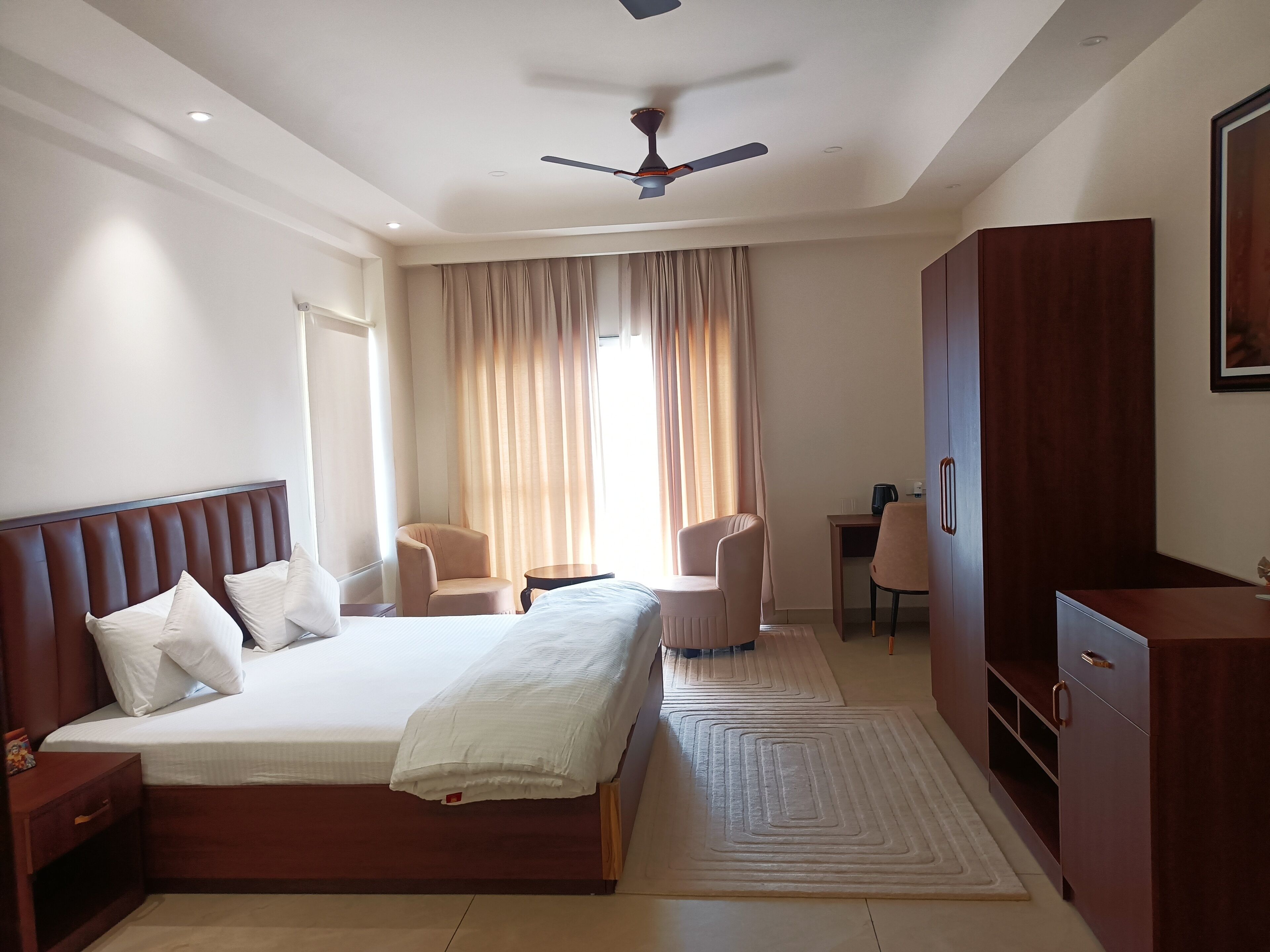 Una habitación de hotel con una cama grande, dos sillones, un escritorio y un armario.