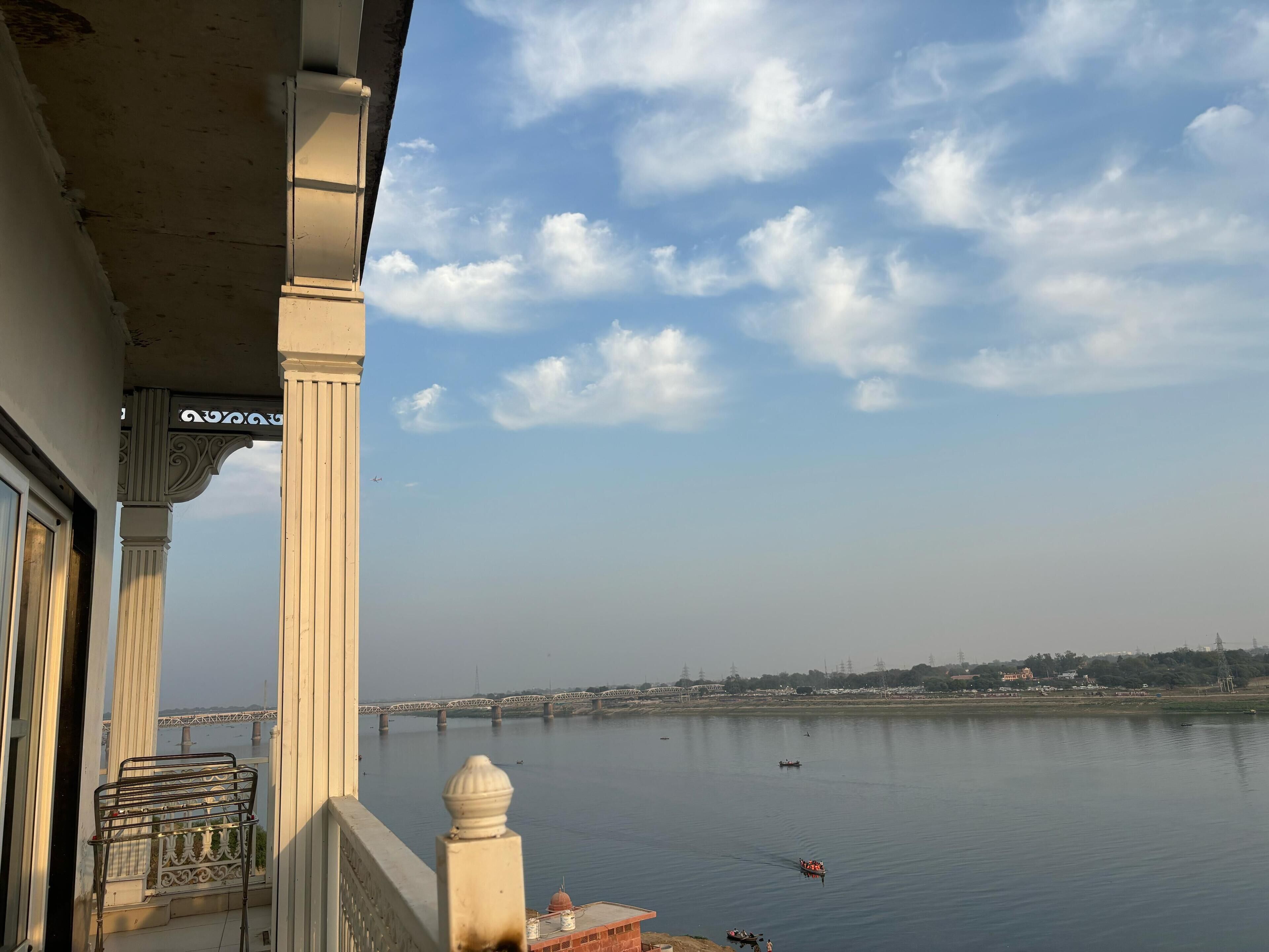 A balcony with a view of a calm river, a bridge in the distance, and a clear sky with clouds.