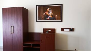 Een kamer met een grote houten garderobe, een klein kastje en een schilderij in een lijst aan de muur.