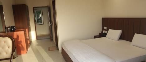 A hotel room with a large bed, a wooden headboard, a desk with a chair, and an air conditioning unit on the wall.
