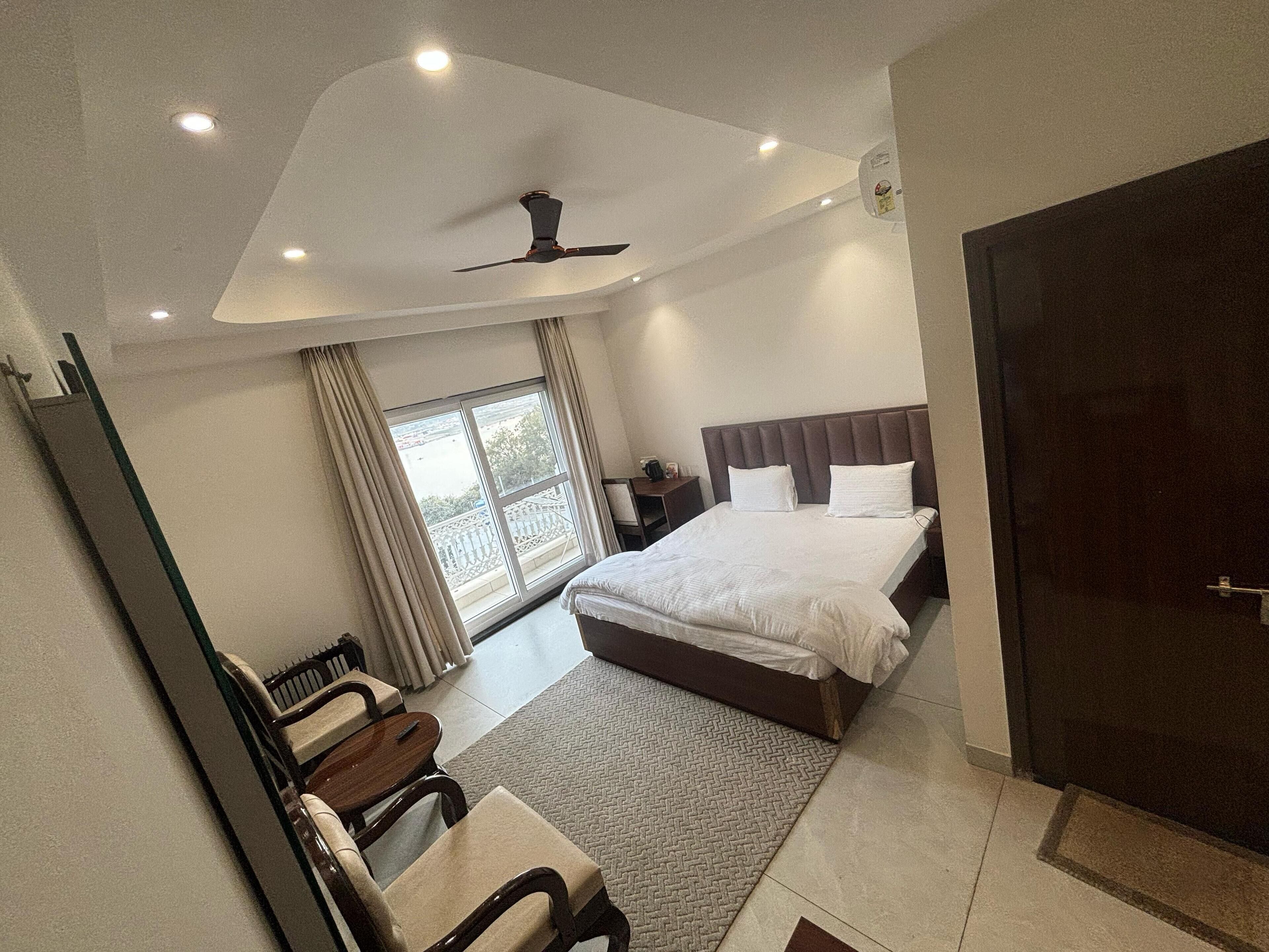 Una habitación de hotel moderna con una cama grande, un escritorio y una silla. Hay una ventana con cortinas, un ventilador de techo y una puerta.