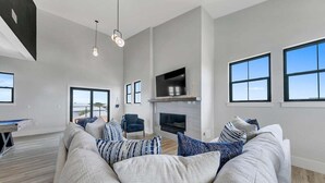 A spacious living room with a large sofa, a fireplace, and a television mounted on the wall. - Sleeps 30! Private Heated Pool, Hot Tub, Game Room, LSV/Golf Cart, GULF VIEWS! Huge! (Santa Rosa Beach)