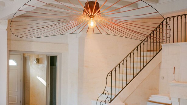 A spacious living area with a curved white sofa, a staircase with a black railing, and a unique ceiling light fixture.