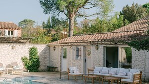 A poolside area with a stone building, outdoor seating, and a large tree.
