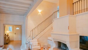 A spacious living room with a fireplace, white furniture, and a staircase leading to an upper level.