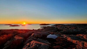 A rocky shoreline at sunset with the sun low on the horizon. - Väderöarnas Värdshus (Fjallbacka)