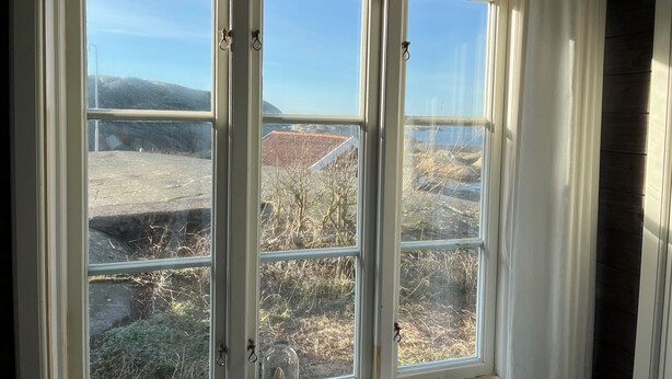 A large window with multiple panes, offering a view of a rural landscape with trees and a building with a red roof. - Väderöarnas Värdshus (Fjallbacka)