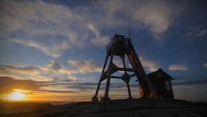 A metal observation tower with a small cabin at its base, overlooking a mountainous landscape during sunset. - Väderöarnas Värdshus (Fjallbacka)