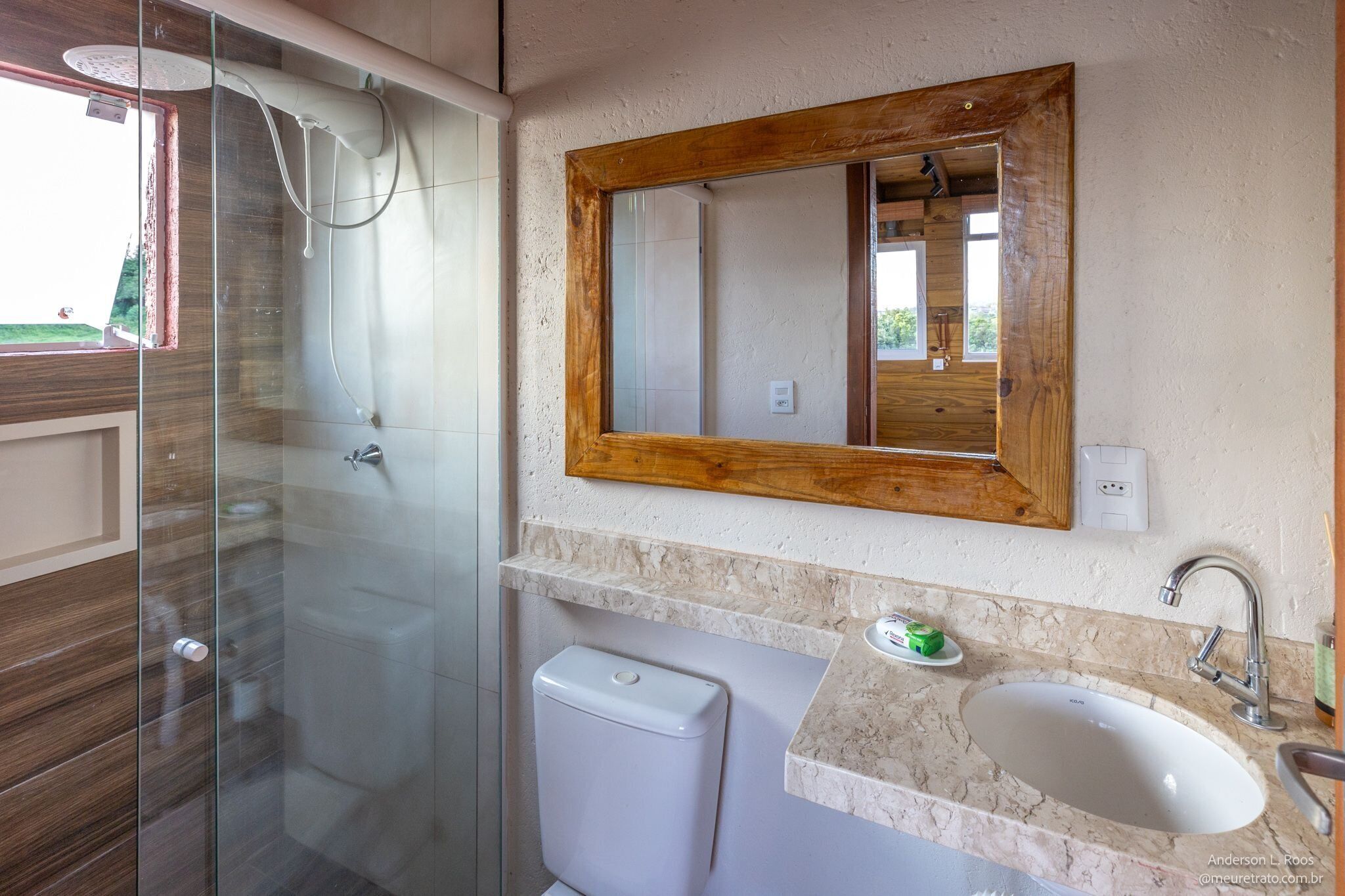 Un baño con ducha de vidrio, un lavamanos blanco y un espejo con marco de madera.