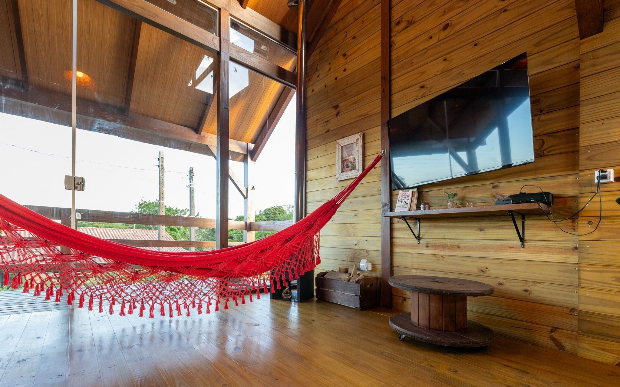 A room with a hammock, wooden walls, a TV, and a round table.
