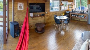 Interior acogedor de una cabaña con detalles de madera, un comedor, un televisor montado en la pared y una hamaca roja.