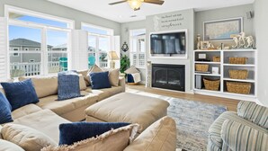 Un salon avec un canapé d’angle beige, une cheminée, un ventilateur de plafond et une vue sur les maisons voisines.