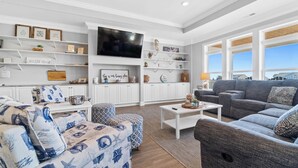 A modern living room with a grey sofa, patterned ottoman, and a flat-screen TV.