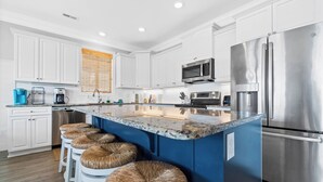 A modern kitchen with white cabinets, a stainless steel refrigerator, a built-in microwave, and a blue island with bar stools.