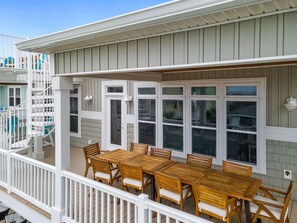 A covered outdoor deck with a wooden table and chairs, white railings, and large windows.