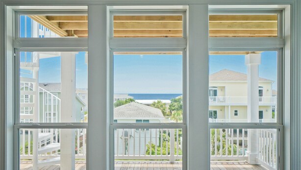 Uitzicht vanaf een balkon met een houten terras, uitkijkend over een kustgebied met huizen en de oceaan.