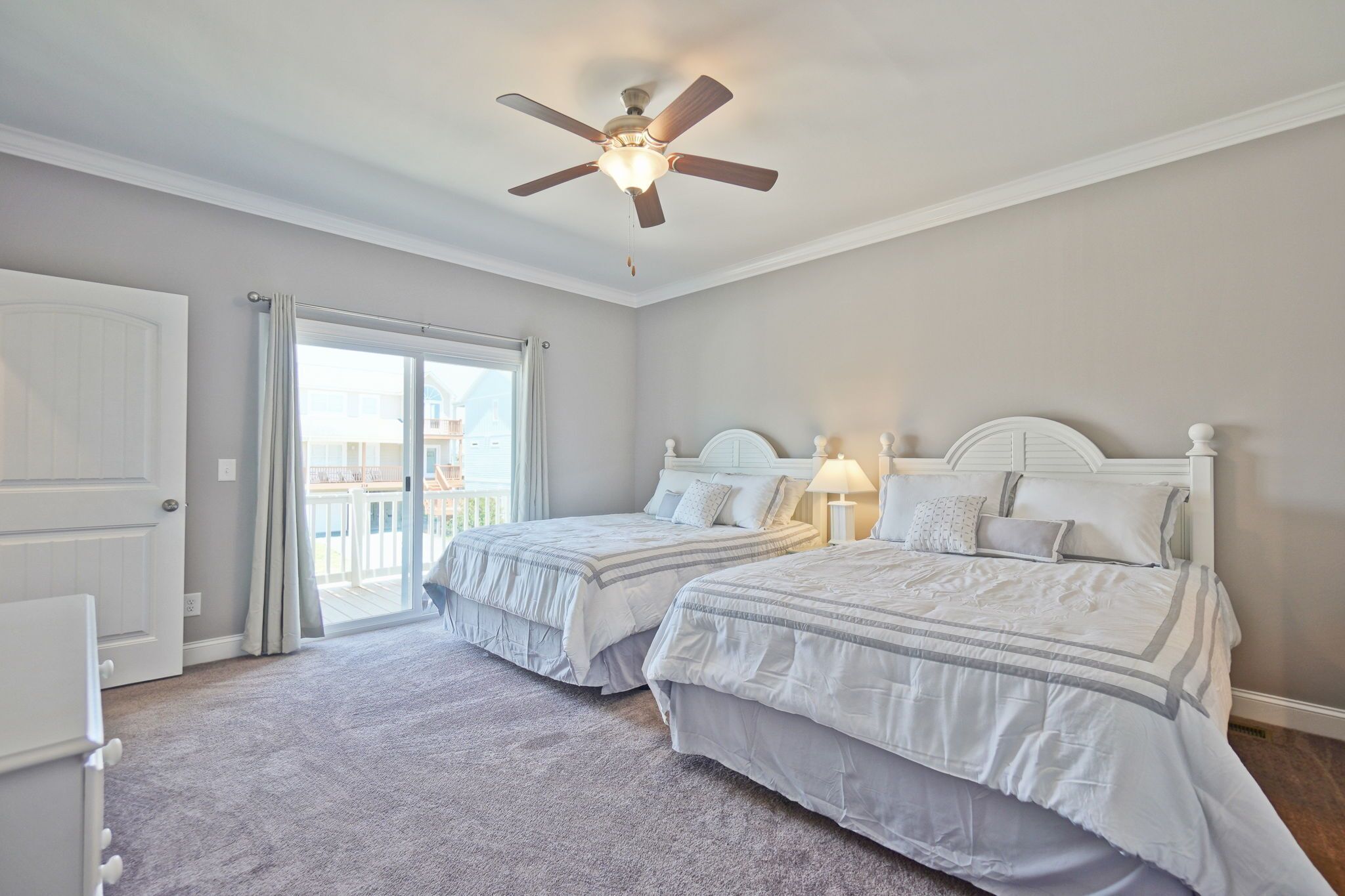 Ein Schlafzimmer mit zwei Betten, einem Deckenventilator, einer Schiebetür zu einem Balkon und einer weißen Tür.