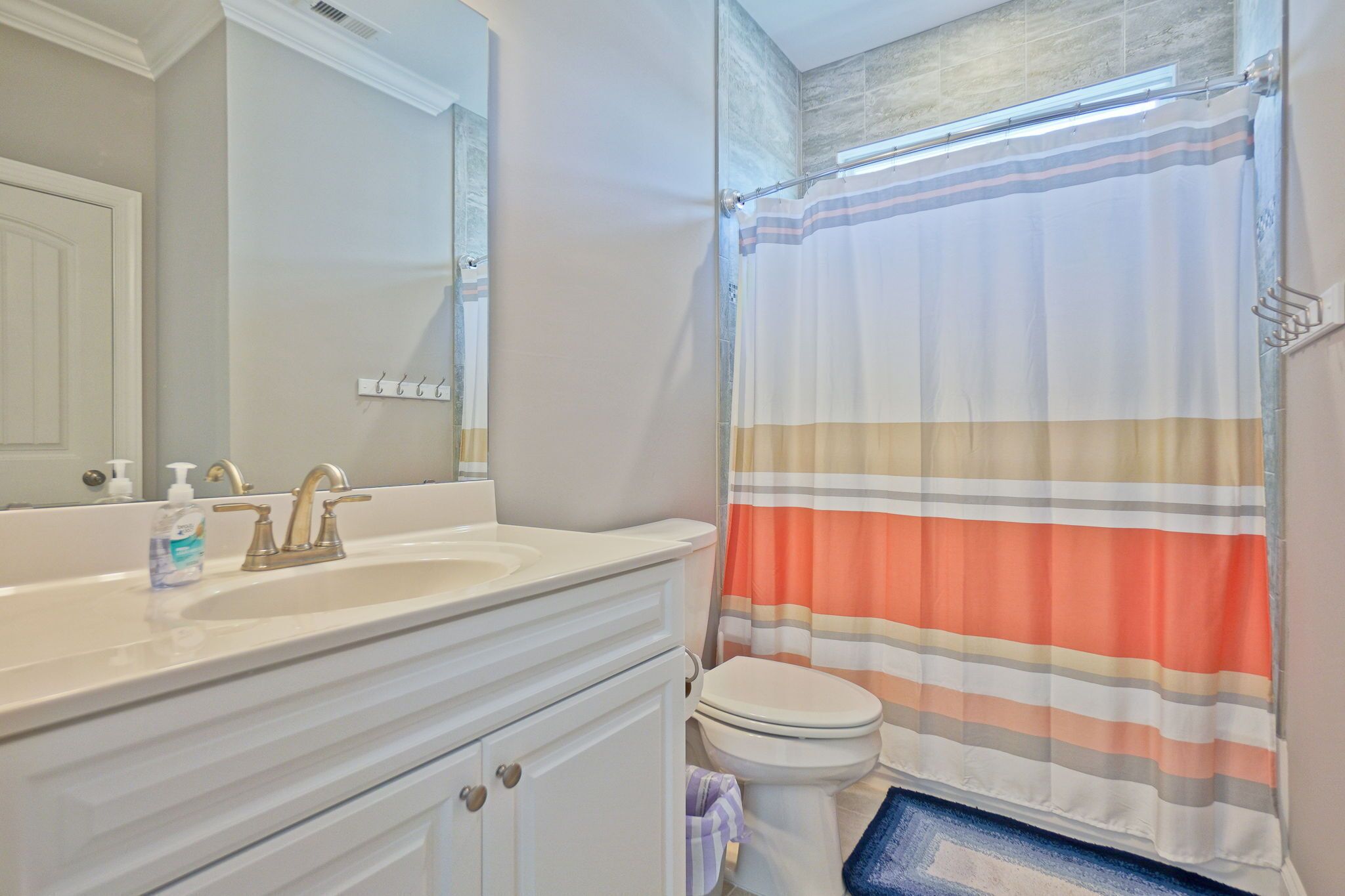 A bathroom with a white sink, a mirror, a toilet, and a shower curtain with horizontal stripes.
