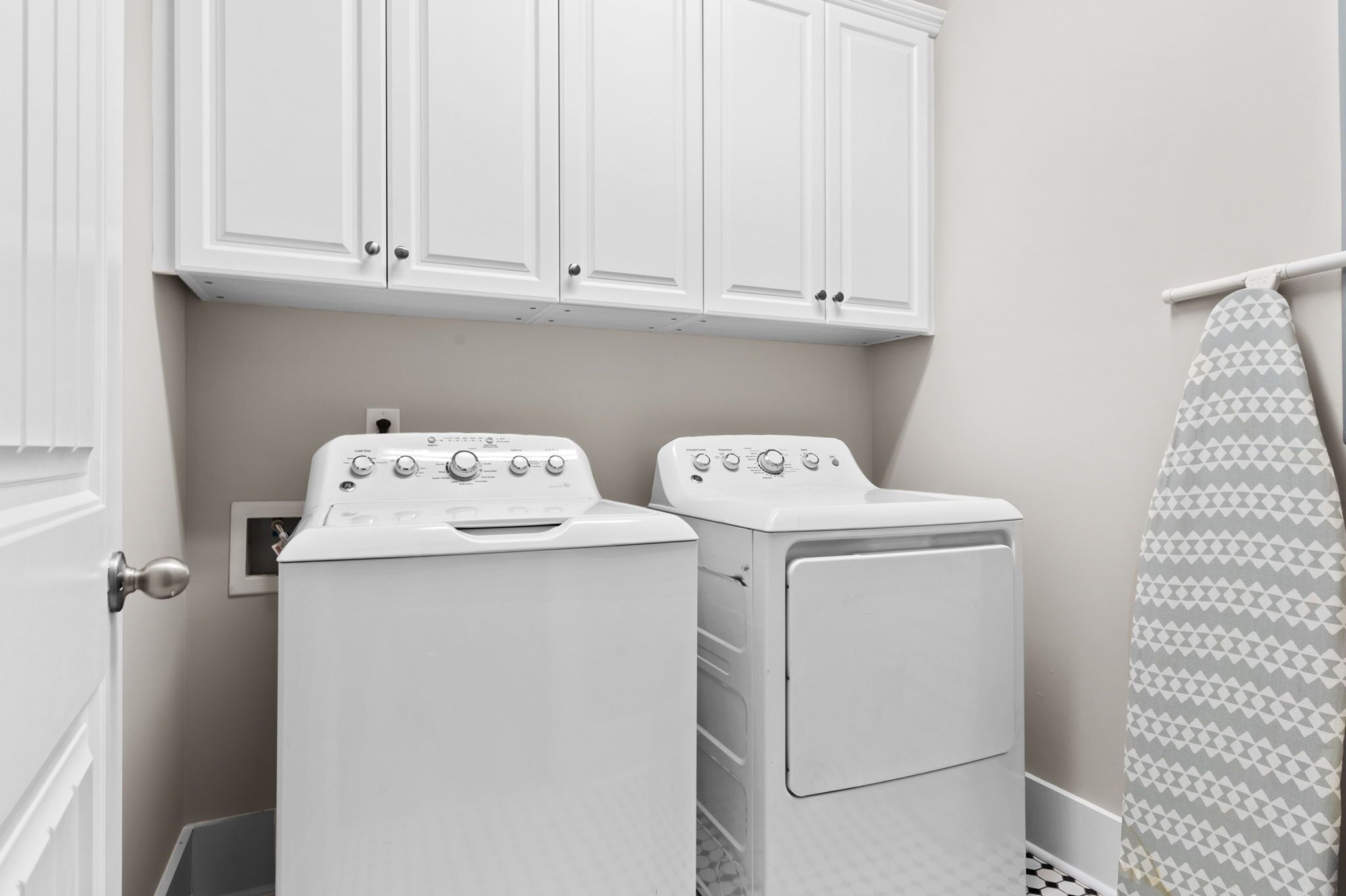 Une buanderie avec deux machines à laver et deux sèche-linge blancs, des placards blancs au-dessus, et un rideau de douche à motifs.