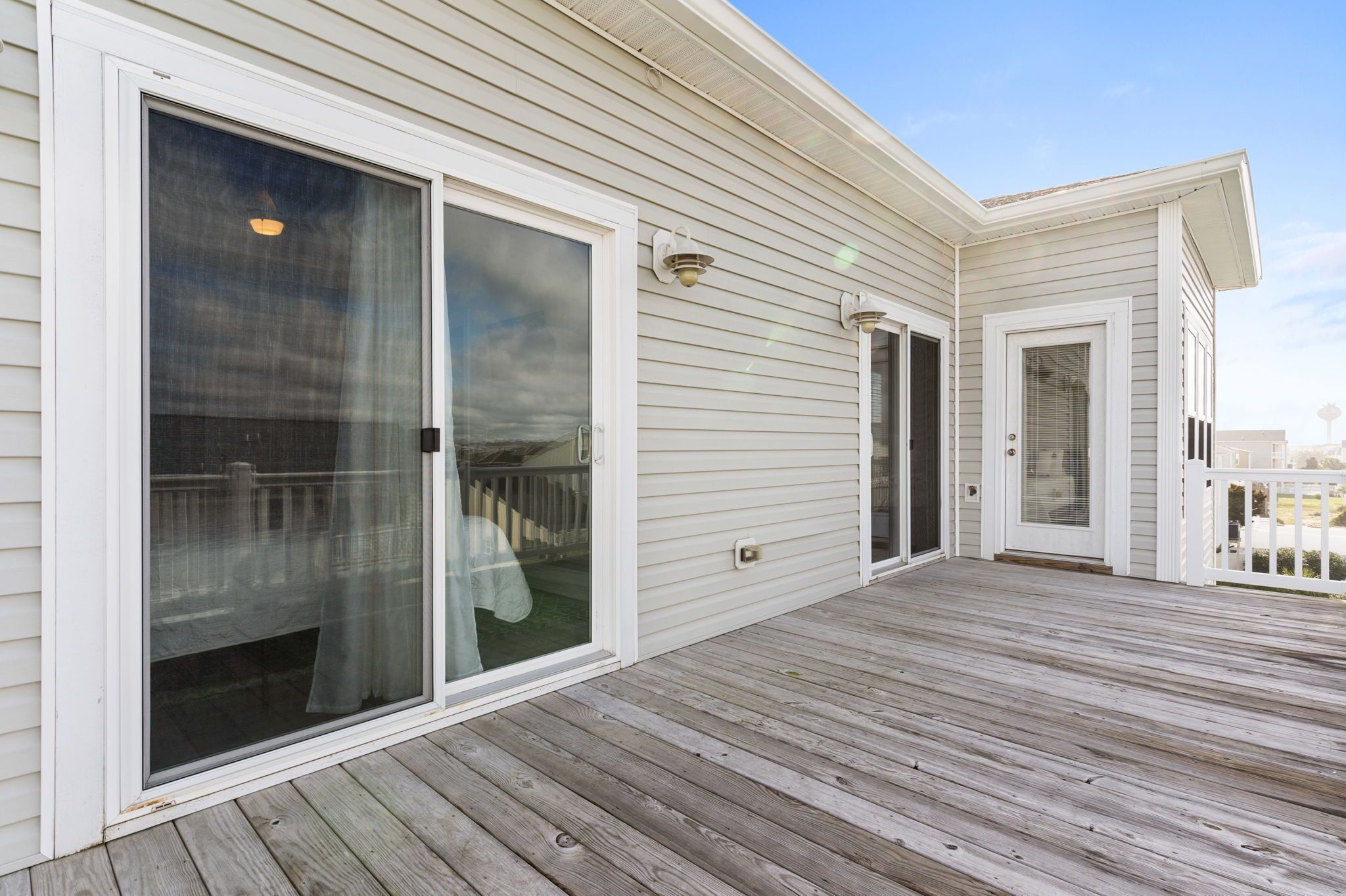 A covered wooden deck with sliding glass doors and a white exterior.