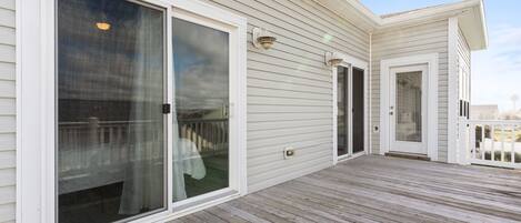 A covered wooden deck with sliding glass doors and a white exterior.