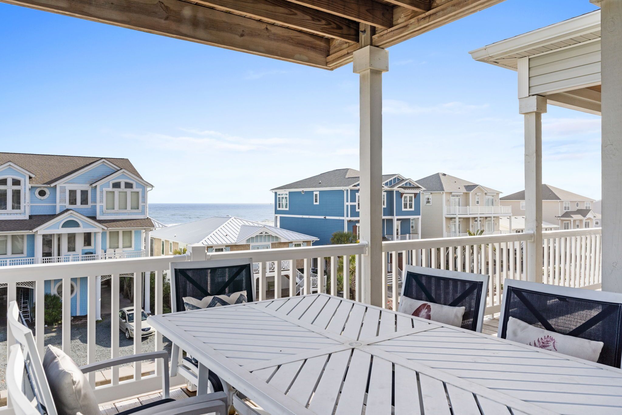 A coastal view from a wooden deck with white railings, overlooking a row of blue and white houses with a clear sky.