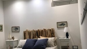 A bedroom with a bed, a nightstand, a lamp, and an air conditioning unit. - Villa Sabbia Granelli (Pachino)