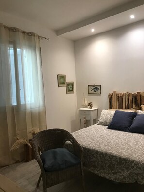A bedroom with a bed, a chair, a small table, and a curtain. - Villa Sabbia Granelli (Pachino)
