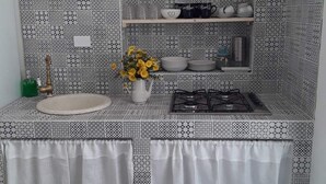 A kitchen with patterned backsplash, white cabinets, and a gas stove. - Villa Sabbia Granelli (Pachino)