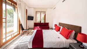 Une chambre avec un grand lit, une chaise, une télévision et une fenêtre avec des rideaux.