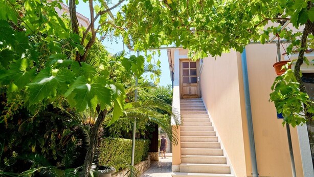 A staircase leading to a building with a beige exterior, surrounded by lush greenery and a potted plant. - Apartment Ady 3 in Mali Lošinj, ideal for two guests. (Mali Losinj)