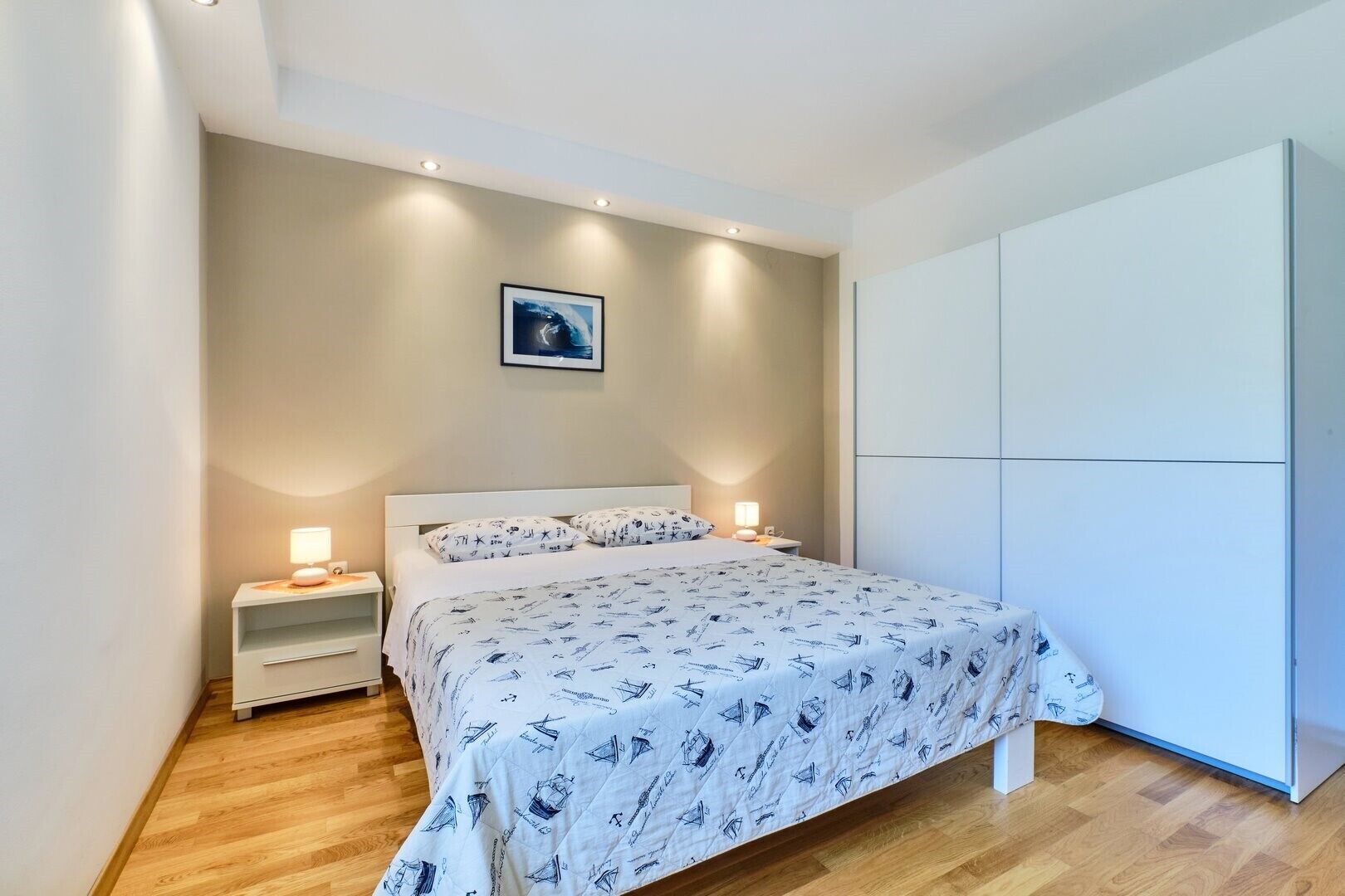 Un dormitorio con cama, mesitas de noche, un armario y un cuadro en la pared.