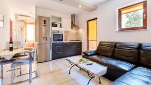 A modern kitchen with stainless steel appliances, a dining area with a table and chairs, and a leather sofa in a living area. - Apartment Ady 3 in Mali Lošinj, ideal for two guests. (Mali Losinj)