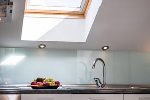 A modern kitchen with a skylight, a stainless steel sink, and a bowl of fruit on the counter.