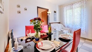 Un comedor con una mesa lista para dos, un florero con flores y una botella de vino.