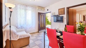 Una habitación con una cama, un comedor con sillas rojas, un televisor en la pared y una ventana con cortinas.