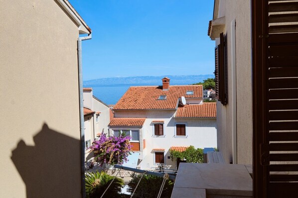A view of a coastal town with terracotta-roofed buildings, a clear blue sky, and a body of water in the distance.
