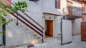A courtyard with stone flooring, a wooden staircase, a white door, and a small table with a chair.