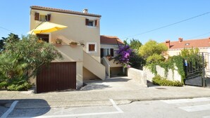 A two-story building with a yellow umbrella, a brown gate, and a small garden with purple flowers. - Apartment Orhideja 1 in Mali Lošinj , the nearest beach Zagazinjine is 500 m away. (Mali Losinj)