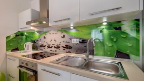 A modern kitchen with white cabinets, a stainless steel sink, and a green leaf-themed backsplash.